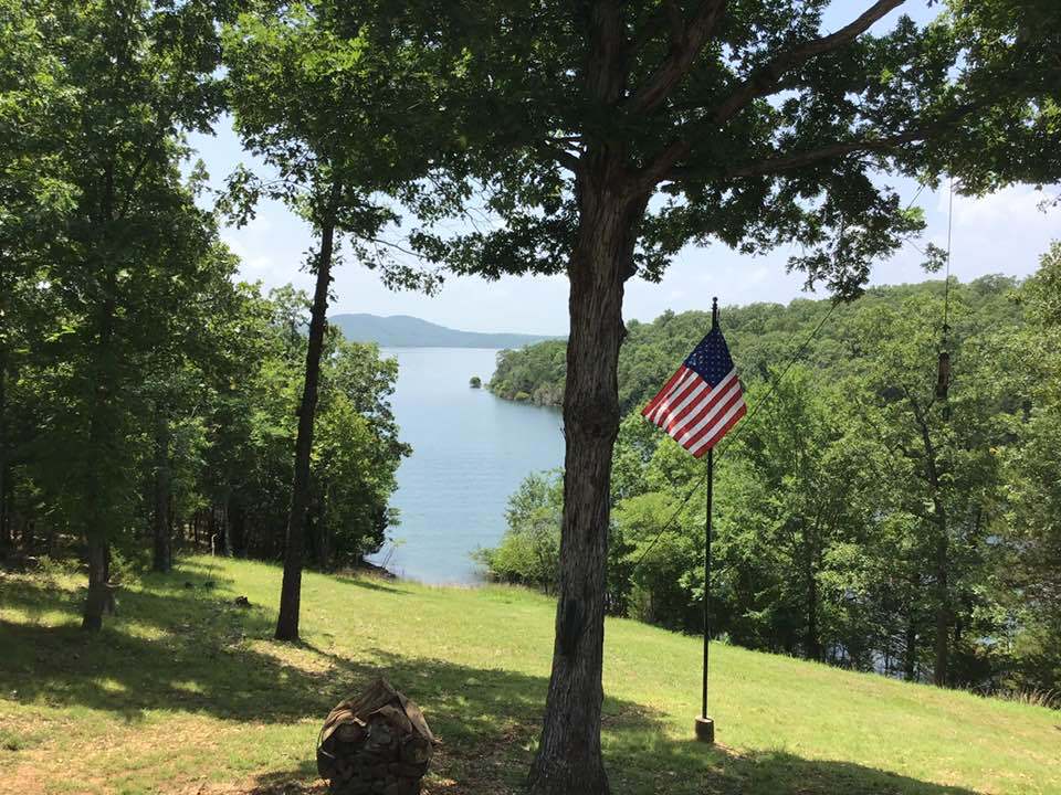 american flag on a grassy field with water and trees in the background